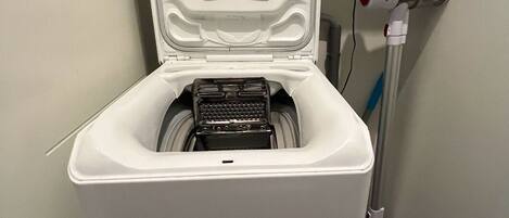 A compact, white portable toilet with a lid, a control panel, and a hose.