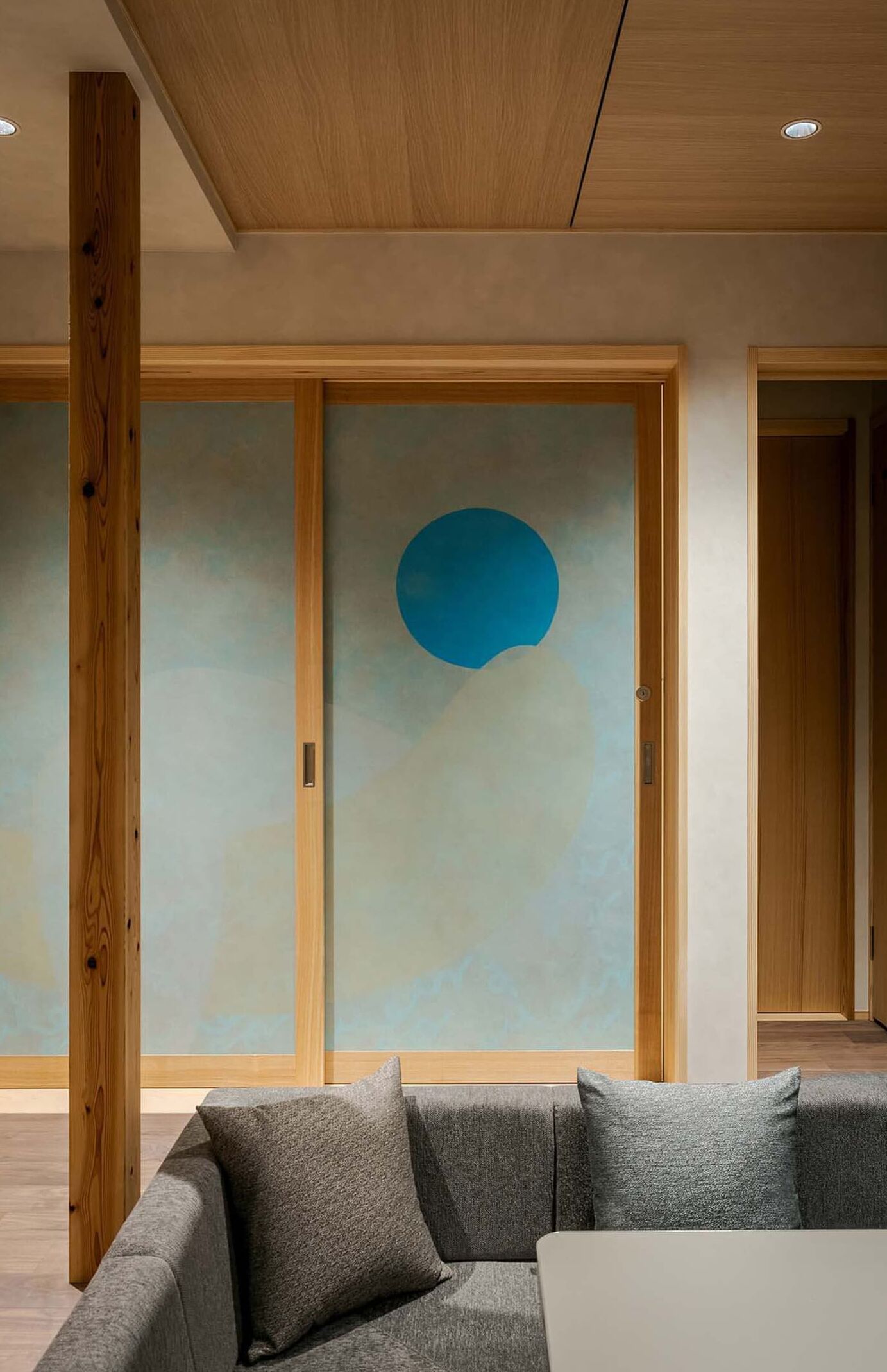 A modern interior with a grey sofa, wooden beams, and a wall with a blue circular design.