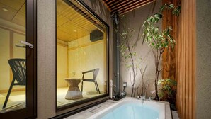 A modern bathroom with a large bathtub, a glass door leading to a seating area, and a small table with a vase.