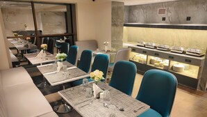 A restaurant with multiple tables set for dining, featuring blue chairs and a buffet area with various dishes. - Maxxvalue Hotel MIDC (Mumbai)