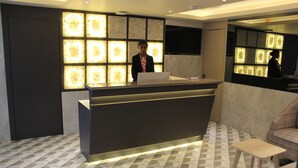A reception desk with a modern design, a seating area with a patterned floor, and a television mounted on the wall. - Maxxvalue Hotel MIDC (Mumbai)