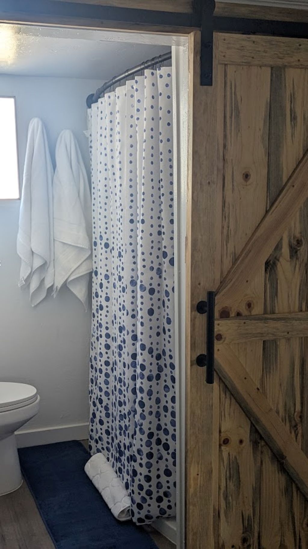 A bathroom with a shower curtain featuring a polka dot pattern, a wooden door, and a white toilet.