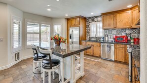 A kitchen with a central island, wooden cabinets, and a stainless steel refrigerator. - Walk to State Farm Stadium! Poolside Desert Escape (Glendale)