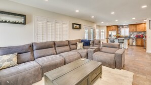 A spacious living area with a large sectional sofa, a coffee table, and a kitchen in the background. - Walk to State Farm Stadium! Poolside Desert Escape (Glendale)