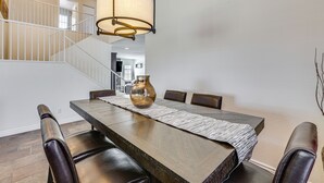 A dining area with a long wooden table, six chairs, a vase, and a hanging light fixture. - Walk to State Farm Stadium! Poolside Desert Escape (Glendale)