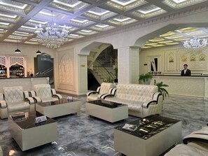 A spacious lobby with a grand chandelier, a reception desk, and a staircase leading to an upper level.