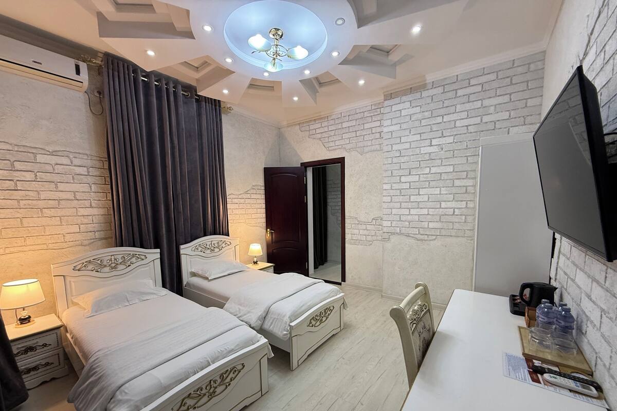 Habitación de hotel con dos camas, un escritorio, un televisor y una pared de ladrillo.