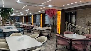 Un restaurante moderno con varias zonas de estar, incluyendo mesas redondas y cabinas, y una escalera que sube a un nivel superior.