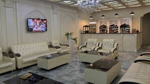 Un lobby lujoso con techo alto, decoraciones ornamentales en las paredes, un televisor y una zona de bar.