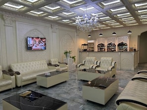 A luxurious lobby with a high ceiling, ornate wall decorations, a television, and a bar area. - Ideal hotel (Samarkand)