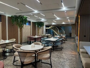 A modern dining area with round tables and cushioned chairs, a staircase in the background, and a patterned floor.