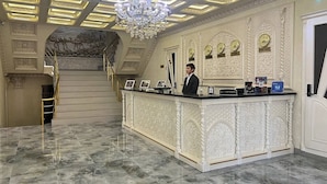 Un área de recepción con suelo de mármol, un mostrador de recepción, un candelabro y una escalera que lleva a un nivel superior.