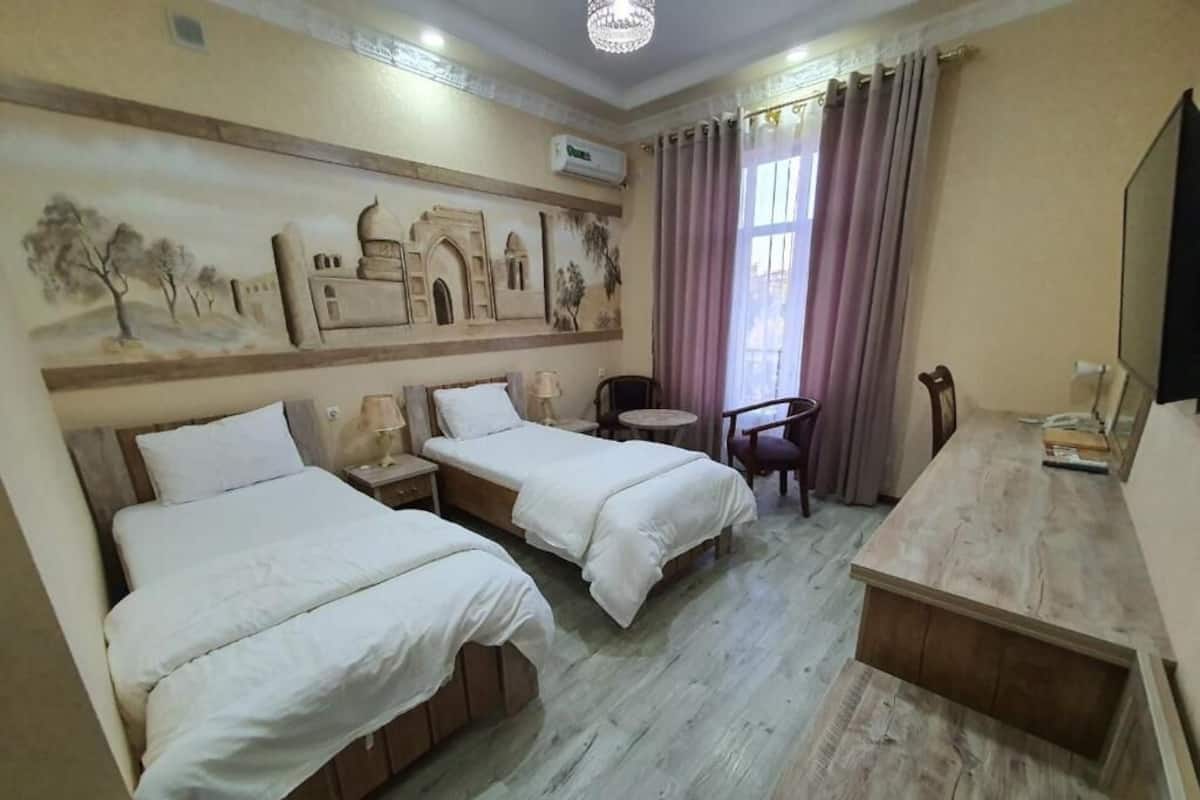 Habitación de hotel con dos camas, una mesita, una silla, un televisor y un detalle decorativo en la pared.