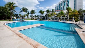 A swimming pool with clear blue water, surrounded by palm trees and lounge chairs. - Vacation getaway with beach access & balcony (CancÃºn)