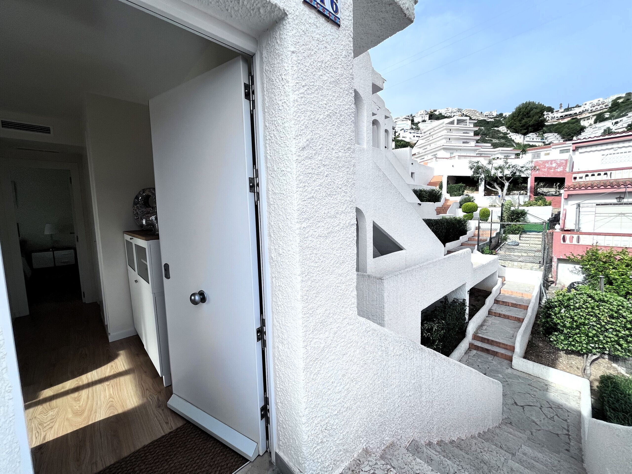 A white door leading to a balcony with a view of a hillside residential area.