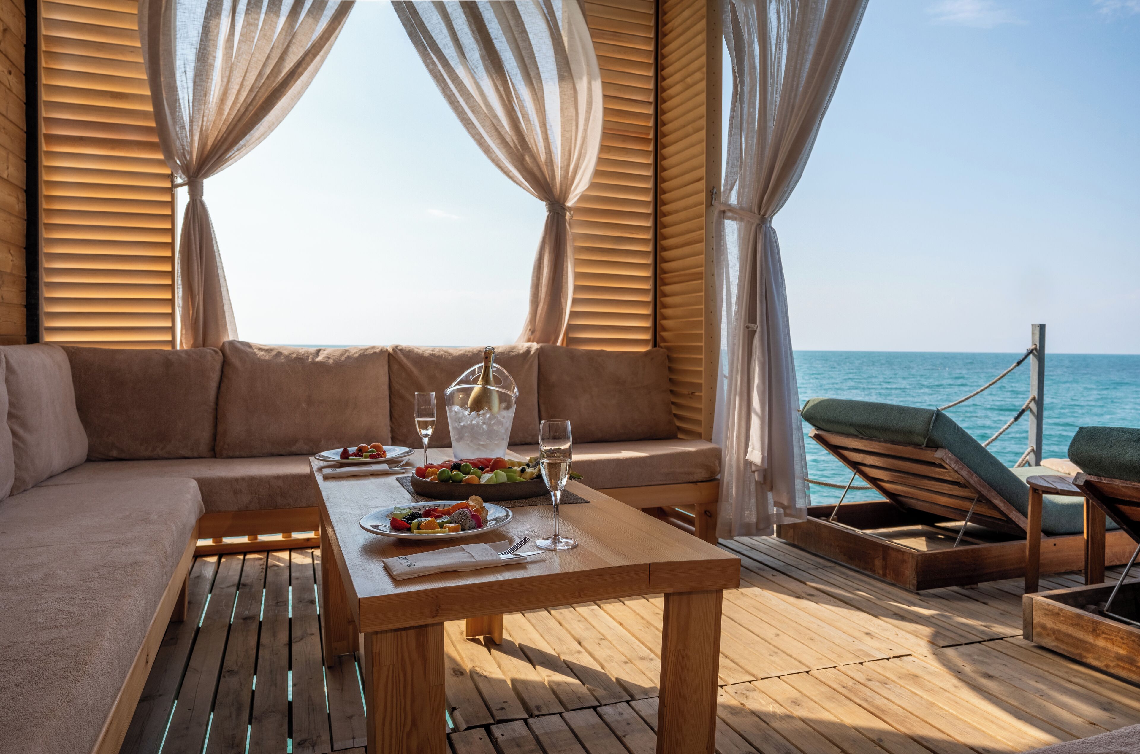 A wooden deck with a sofa, lounge chairs, and a table set with food and drinks.
