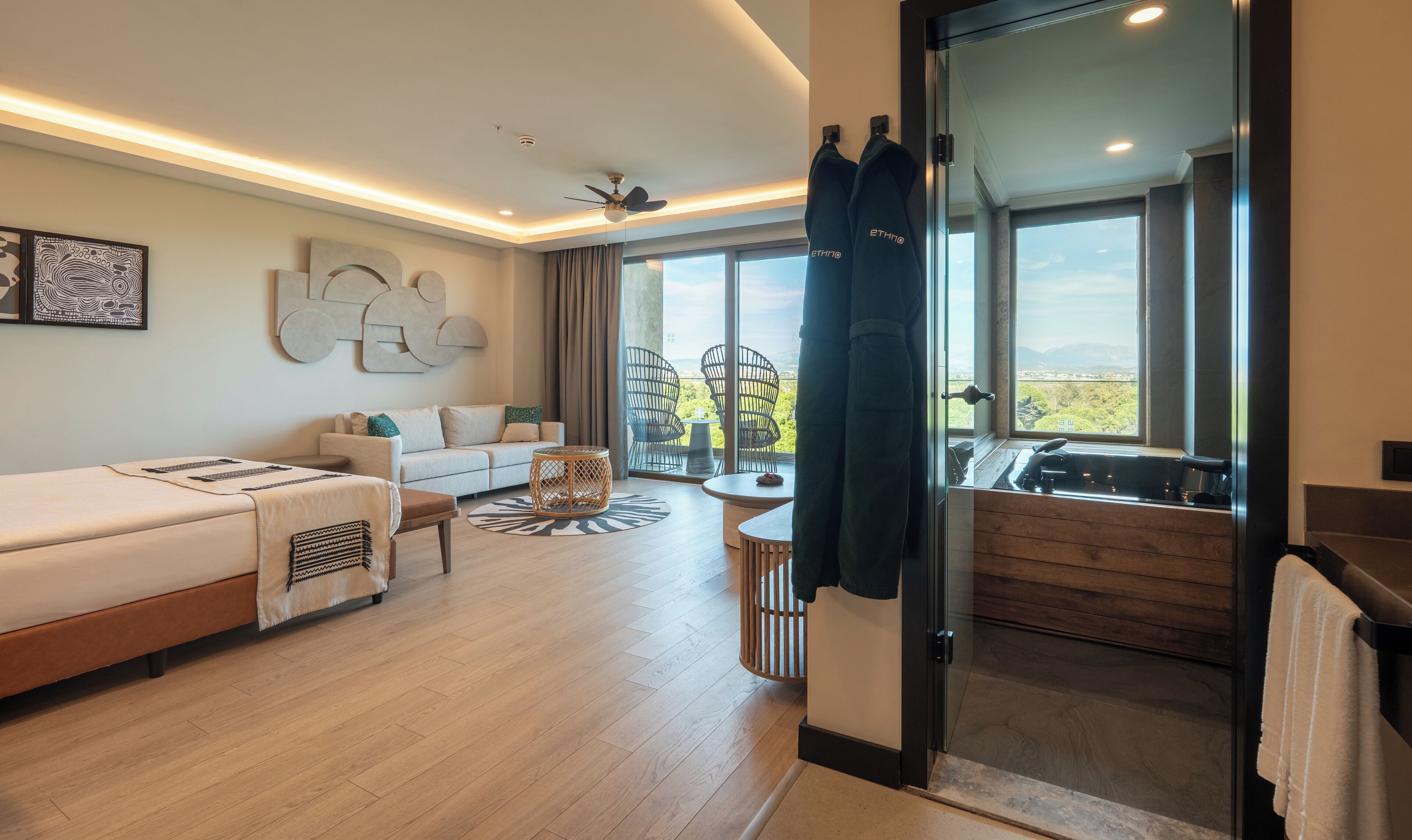 Een moderne hotelkamer met een bank, een klein rond tafeltje, een bed, een balkon met uitzicht en een douche.