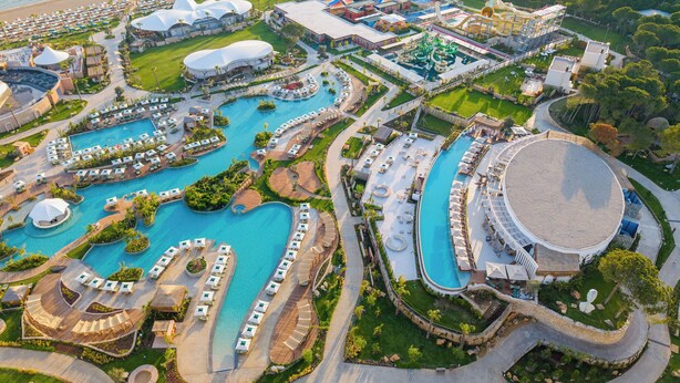 An aerial view of a resort with multiple swimming pools, a large circular building, and a water park. - Ethno Belek (Serik)