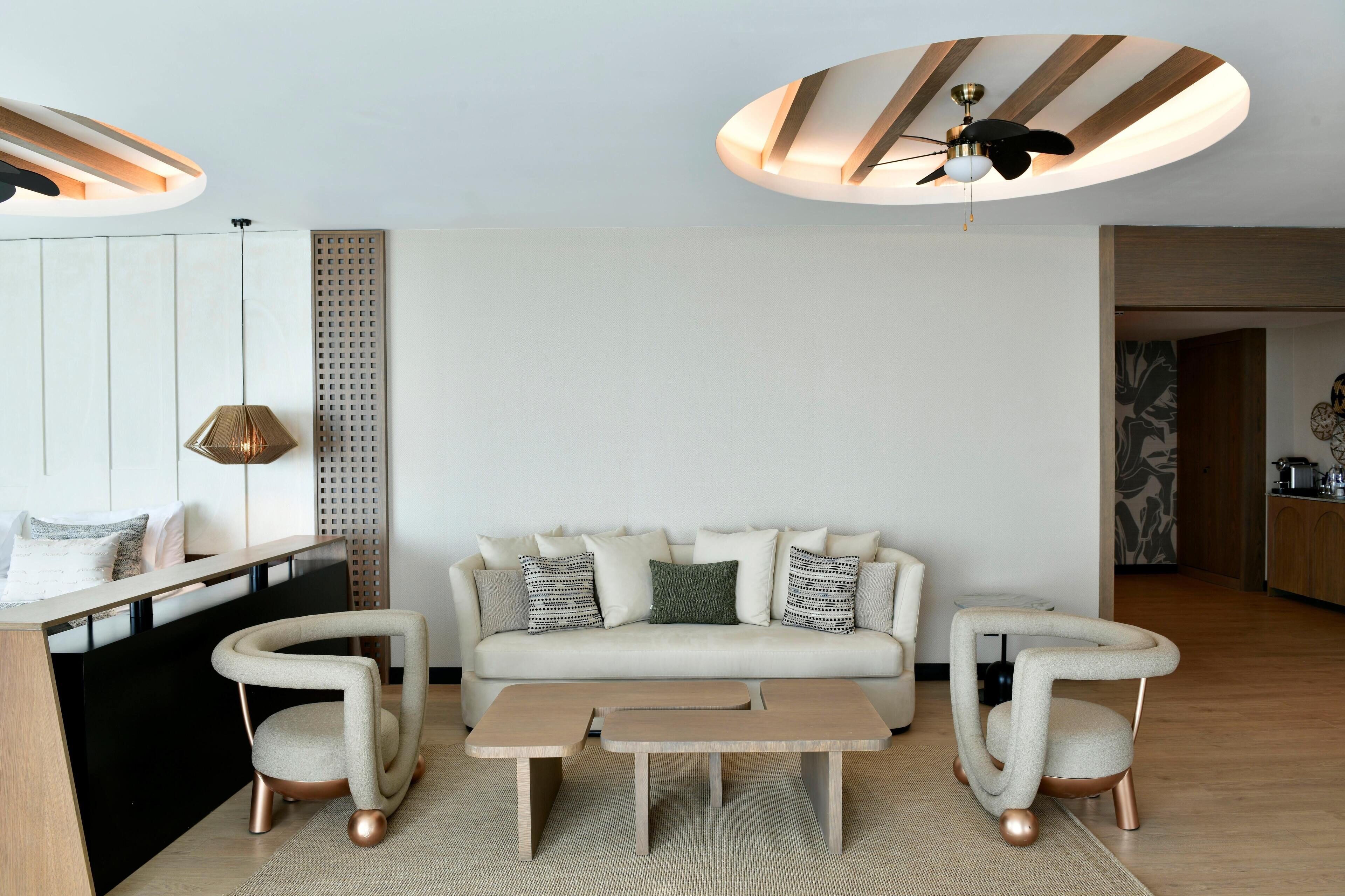 Una sala de estar moderna con un sofá, dos sillones, una mesa de centro, un ventilador de techo y una lámpara colgante.