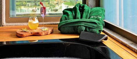 A window seat with a view of the sea, a green towel, a glass of drink, and a wooden tray.