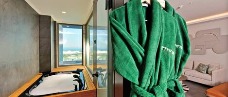 A modern bathroom with a wooden bathtub, a green robe hanging on a rack, and a view of the city through large windows.