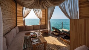 A wooden deck with a sofa, a dining table with plates and a bottle, and a lounge chair. - Ethno Belek (Serik)