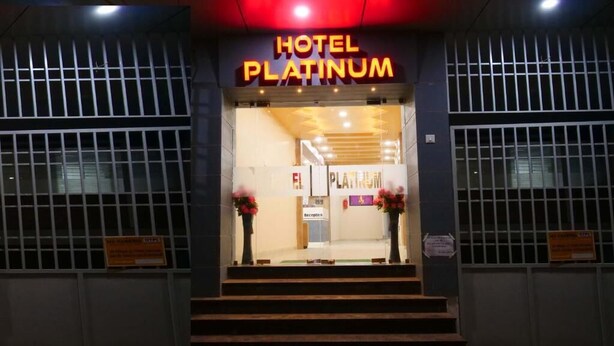 L’entrée de l’hôtel Platinum se compose d’un comptoir de réception, d’une enseigne au-dessus de la porte et de deux compositions florales de part et d’autre.