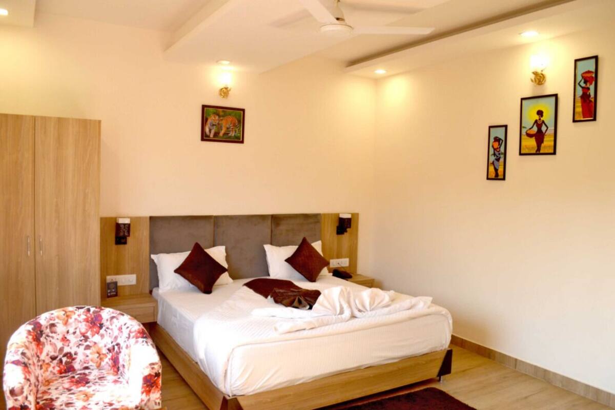 A bedroom with a bed, a wooden wardrobe, a chair, and artwork on the walls.