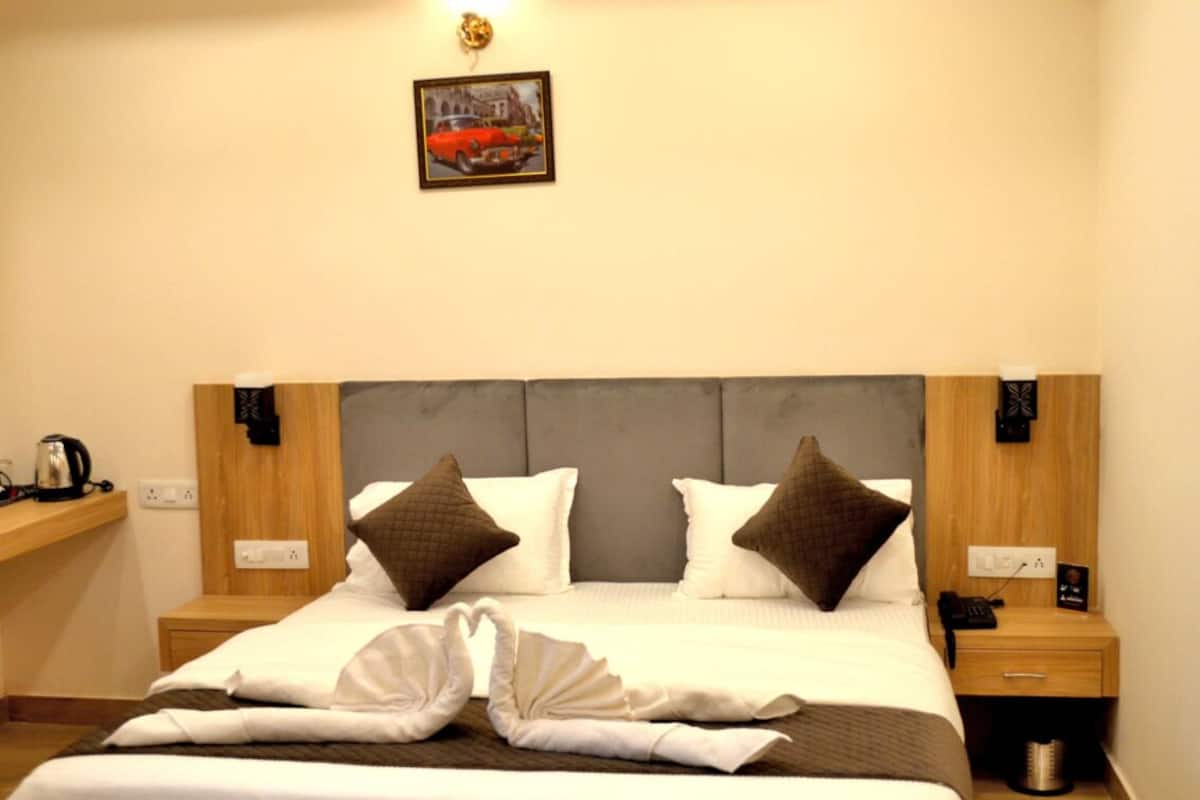 A neatly made bed with white and brown linens, a grey upholstered headboard, and a framed picture on the wall.