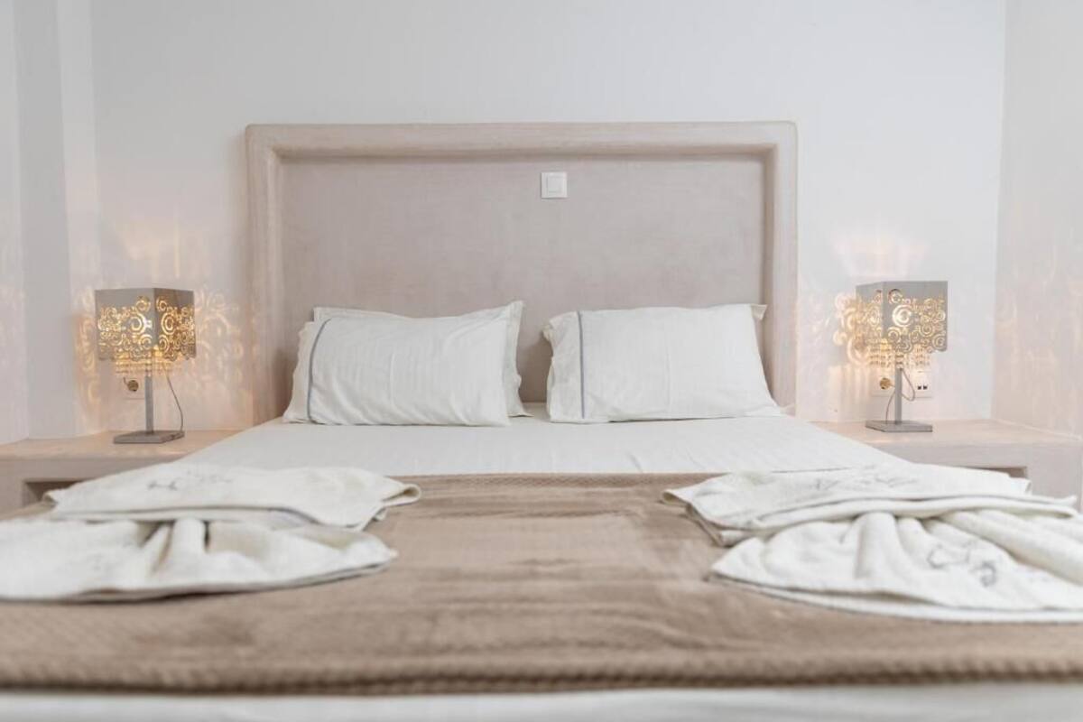 A neatly made bed with white linens and two bedside lamps with decorative light fixtures.