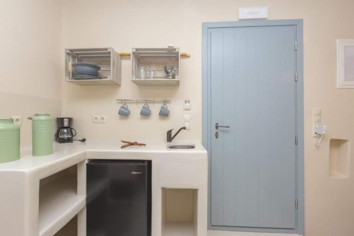 A compact kitchenette with a refrigerator, sink, and storage shelves.