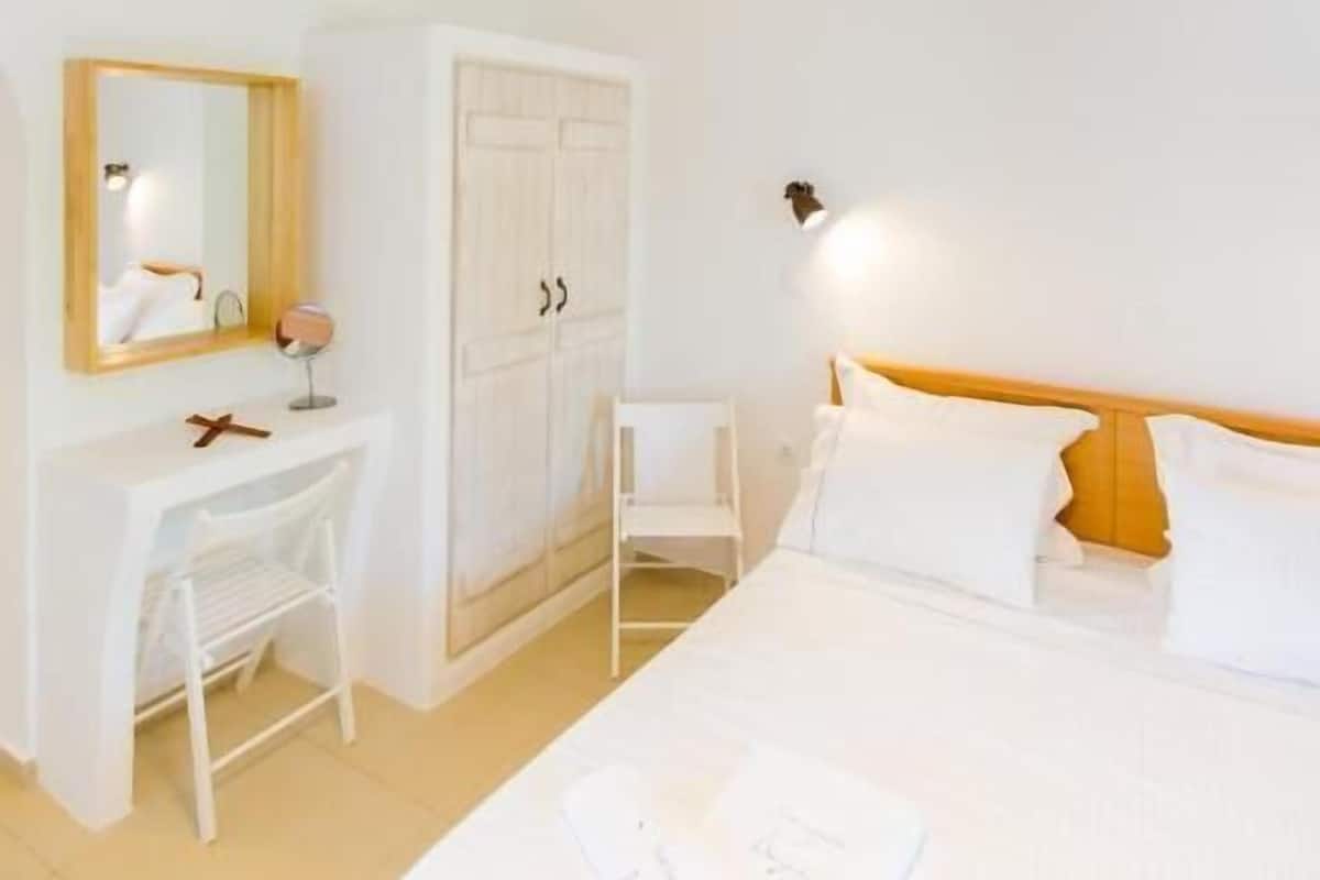 A bedroom with a bed, a desk, a wardrobe, and a hanging light fixture.