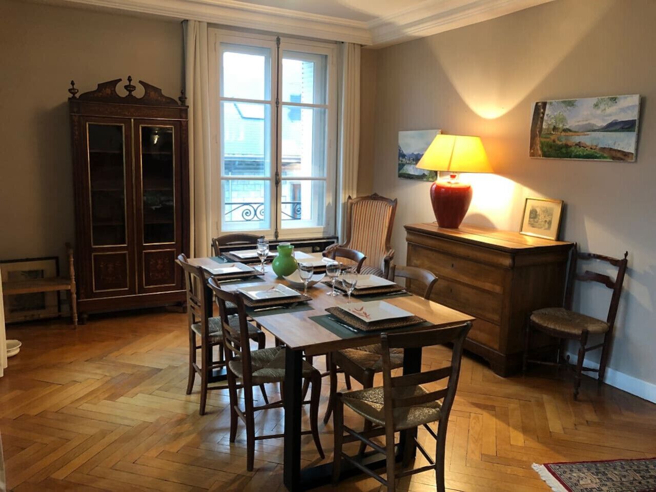 Un coin repas avec une table en bois dressée pour quatre personnes, entourée de chaises, d’un buffet et d’un radiateur.