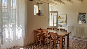 A dining area with a wooden table and chairs, a bookshelf, and a window with curtains. - Cottage (sleeps 6) at Domaine de Chantageasse, a 17th century estate with pool (Asnières-la-Giraud)