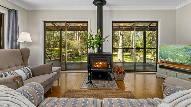 A living room with a wood-burning stove, large windows, a sofa, and a television. - Ellendale - enjoy the serenity (Kurmond)