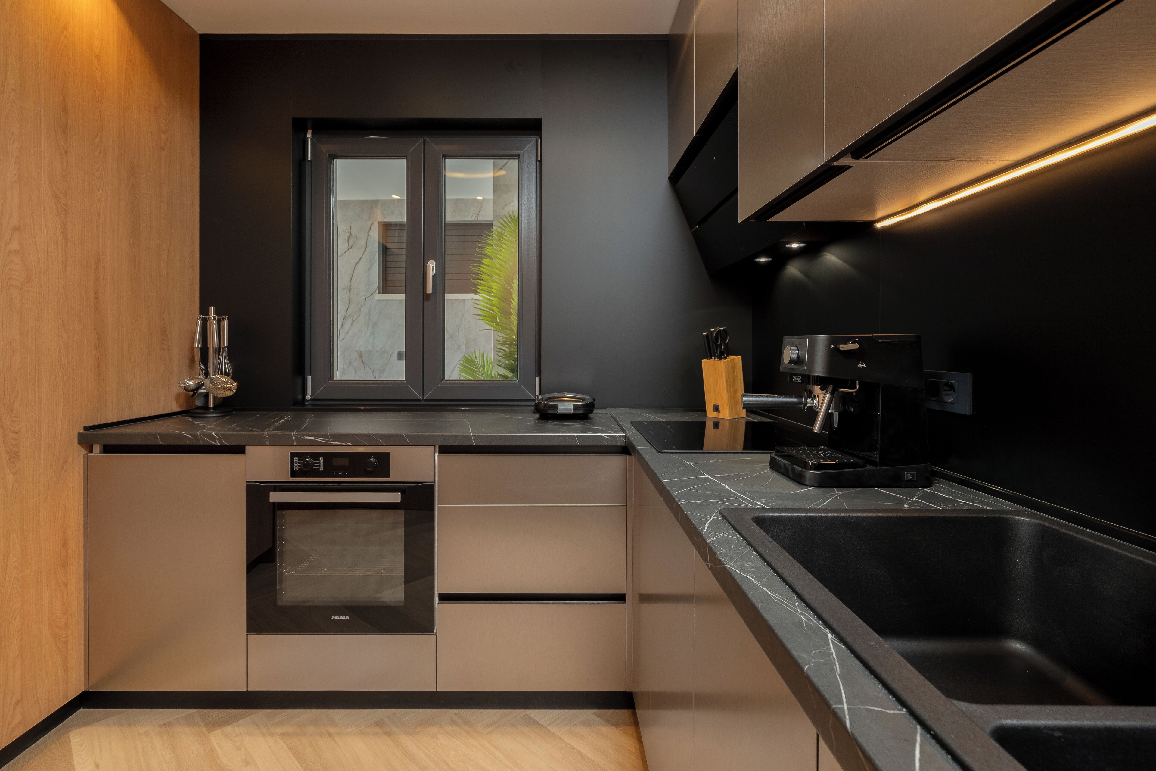 A modern kitchen with a built-in oven, a large sink, and a window with a view of greenery.