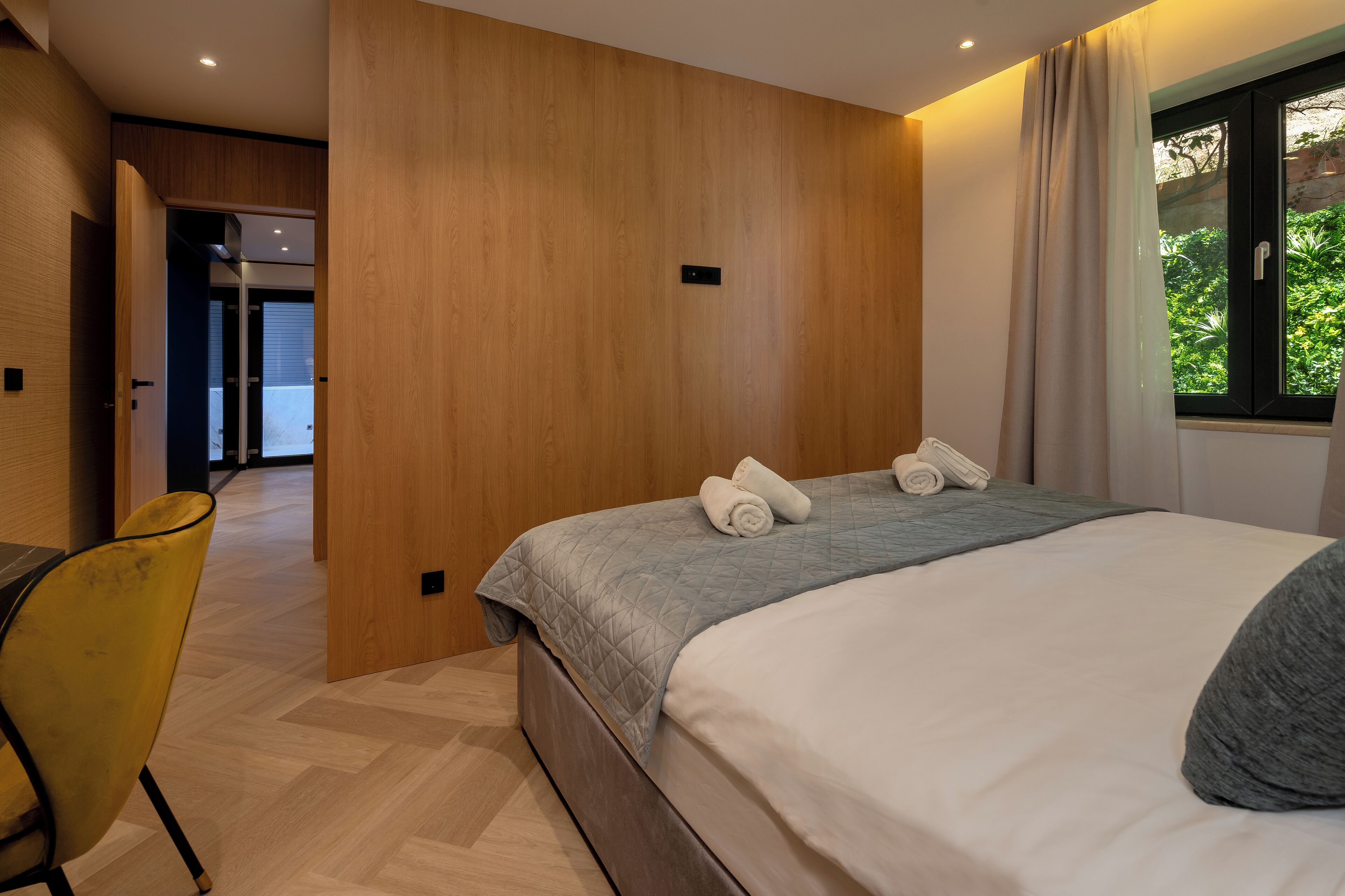 Une chambre d’hôtel moderne, équipée d’un lit, d’un bureau et offrant une vue sur la verdure environnante.