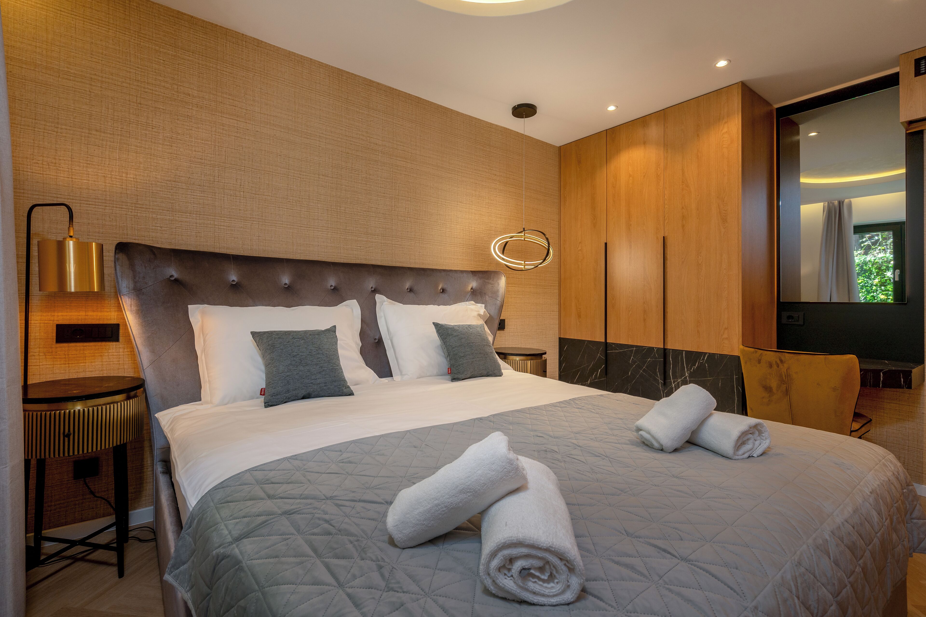 A modern hotel room with a large bed, a round mirror, and a wooden wardrobe.