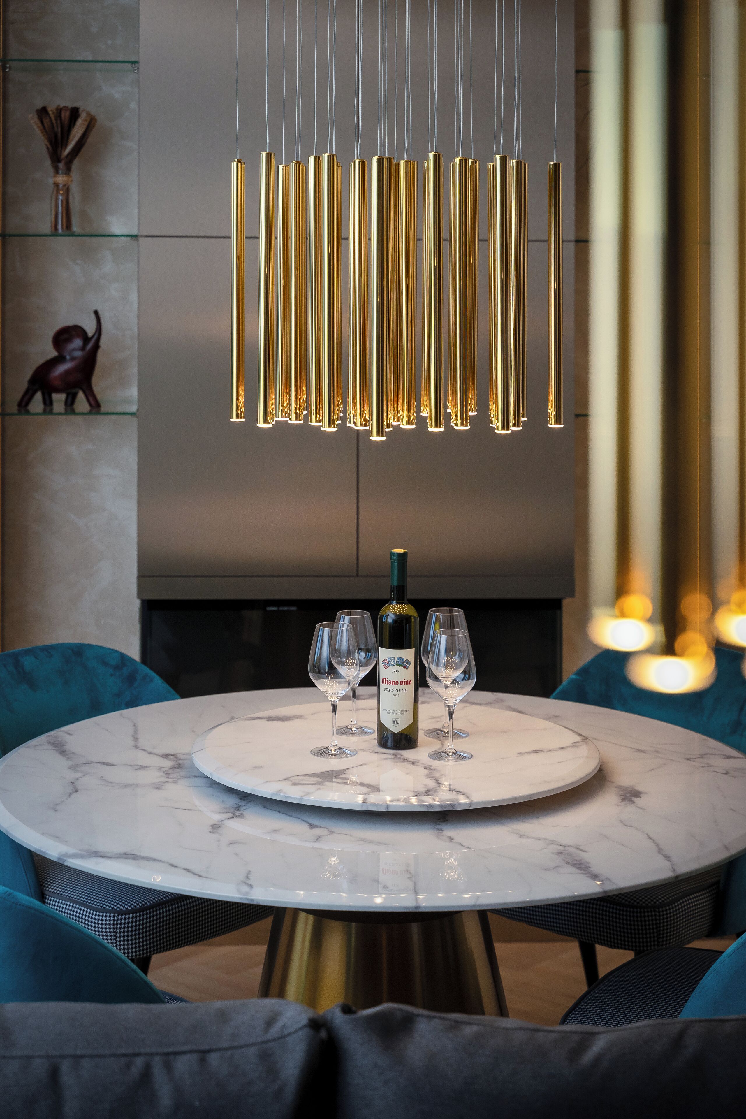 Un comedor moderno con una mesa de mármol, dos sillas, una botella de vino y un elemento decorativo en la pared.
