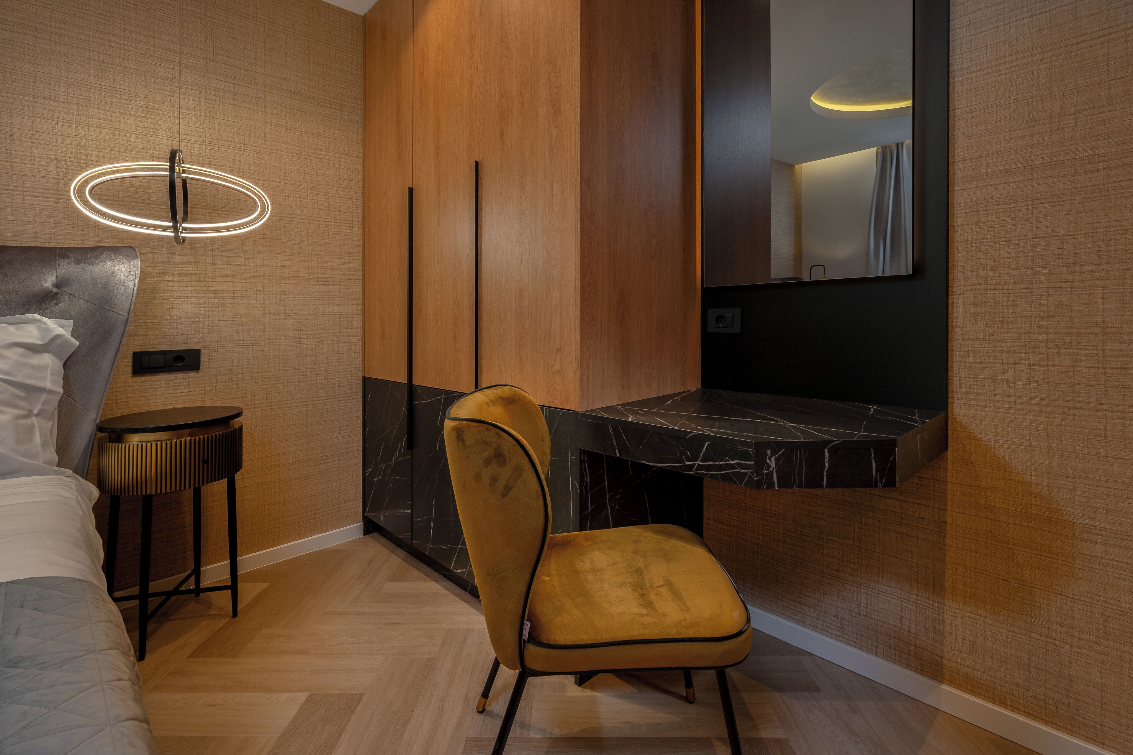Una habitación de hotel moderna con una cama, una pequeña mesa redonda, una silla amarilla, un banco de mármol negro y un espejo montado en la pared.