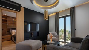 A modern living room with a sofa, ottoman, and a round coffee table. There is a TV mounted on the wall, a ceiling light fixture, and a view of a balcony through large windows. - Old City Viewpoint by Dubrovnik view (Dubrovnik)