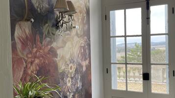 Une pièce décorée d’une grande fresque florale, avec une porte blanche dotée de plusieurs fenêtres et une plante en pot.