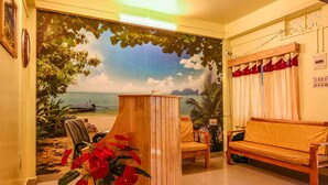 A room with a beach mural, a wooden desk, a sofa, and a chair. - Kanchan's Nest Homestay (Port Blair)
