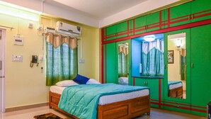A bedroom with a wooden bed, a green wardrobe with a mirror, and an air conditioning unit on the wall. - Kanchan's Nest Homestay (Port Blair)