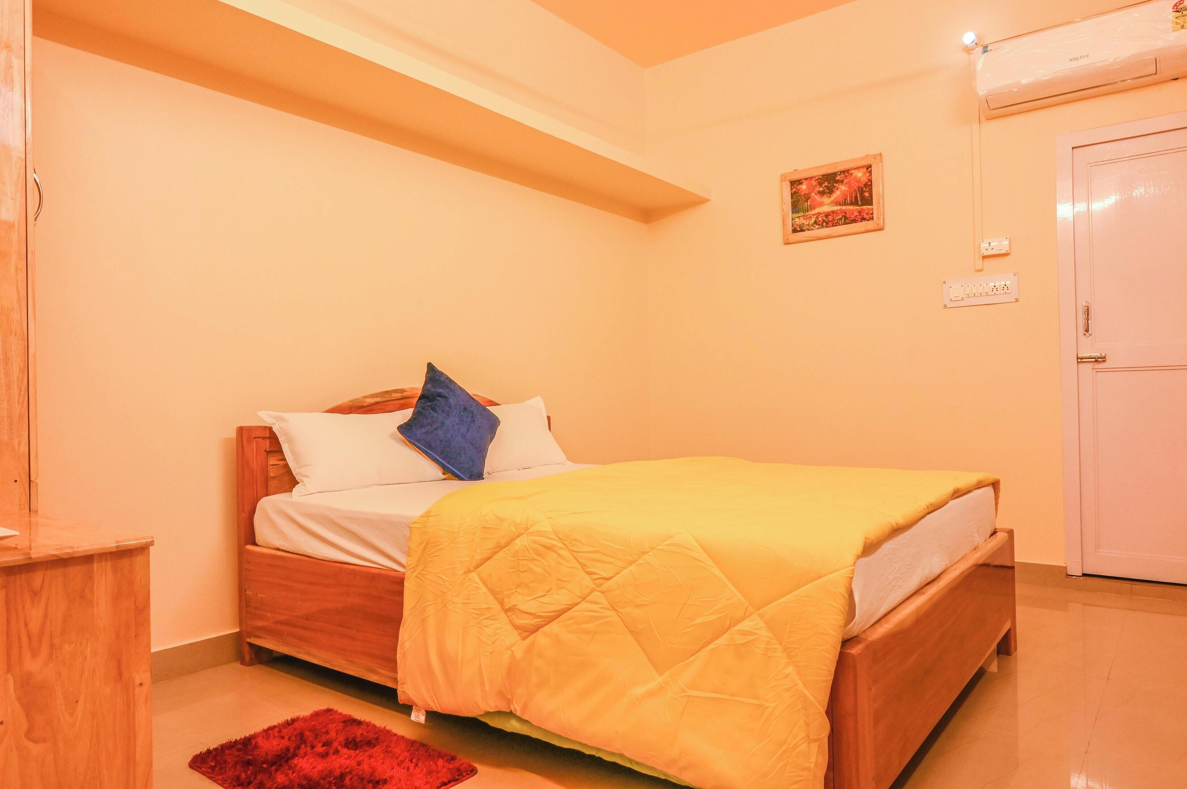 Un dormitorio con una cama de madera, una alfombra roja, una puerta blanca y un aire acondicionado fijado a la pared.