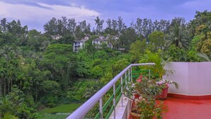 A balcony with a view of a lush green landscape, a red tiled floor, and potted plants. - Kanchan's Nest Homestay (Port Blair)