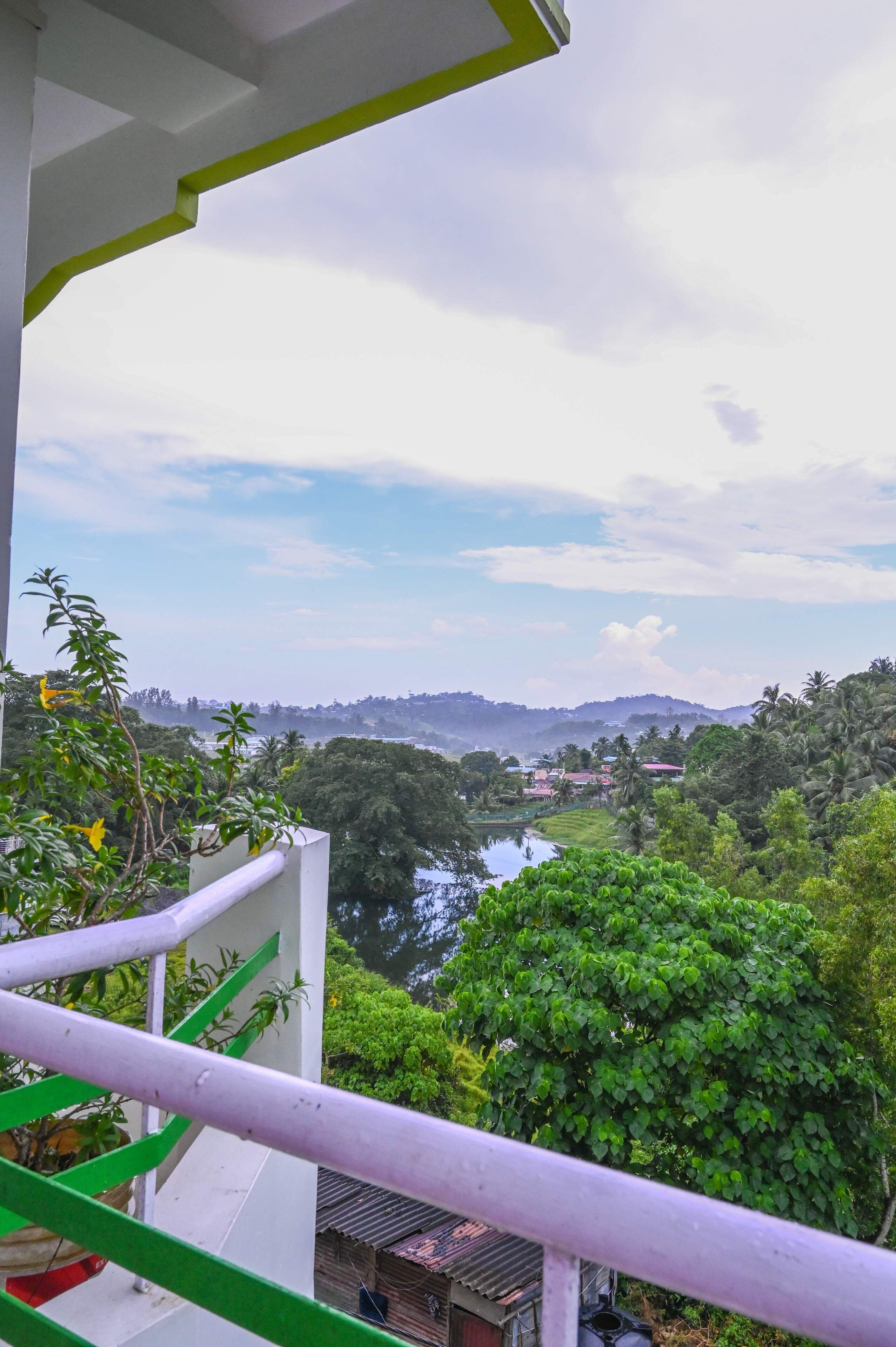 A balcony with a view of a river, greenery, and distant hills.