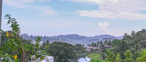 A balcony with a view of a river, greenery, and distant hills.