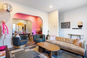 A modern living room with a sofa, two armchairs, a coffee table, and a dining area with a table and chairs.