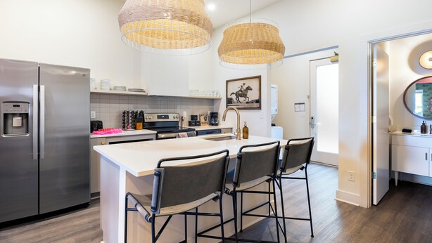 A modern kitchen with stainless steel appliances, a large island with bar stools, and wicker pendant lighting. - Curated Bachelorette Retreat w/ Balcony, Glam Room, Roof | Close to Downtown! (Nashville)
